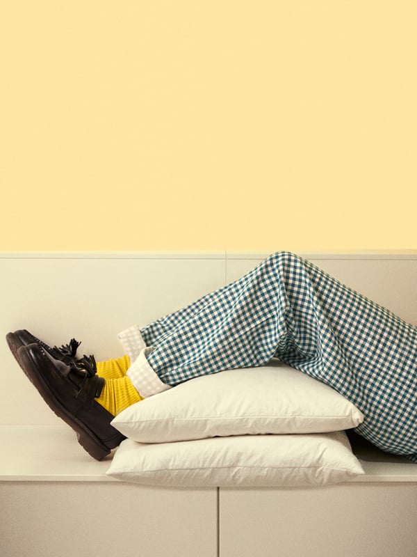 A person wearing a green pyjama is resting his legs on two white pillows while wearing black shoes and socks.