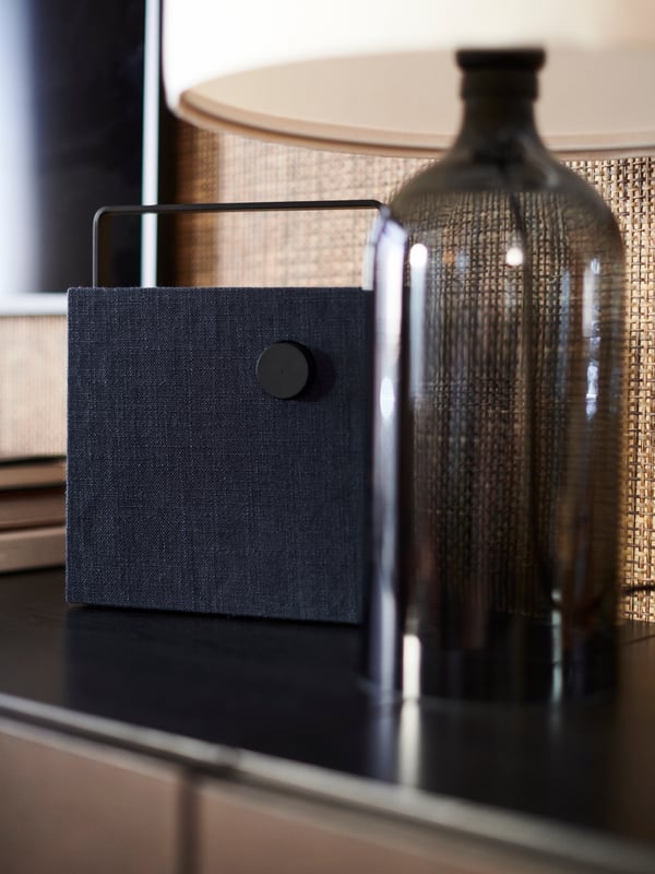 A TONVIS table lamp with a smoked glass base and white shade on a dark surface beside an ENEBY bluetooth speaker.