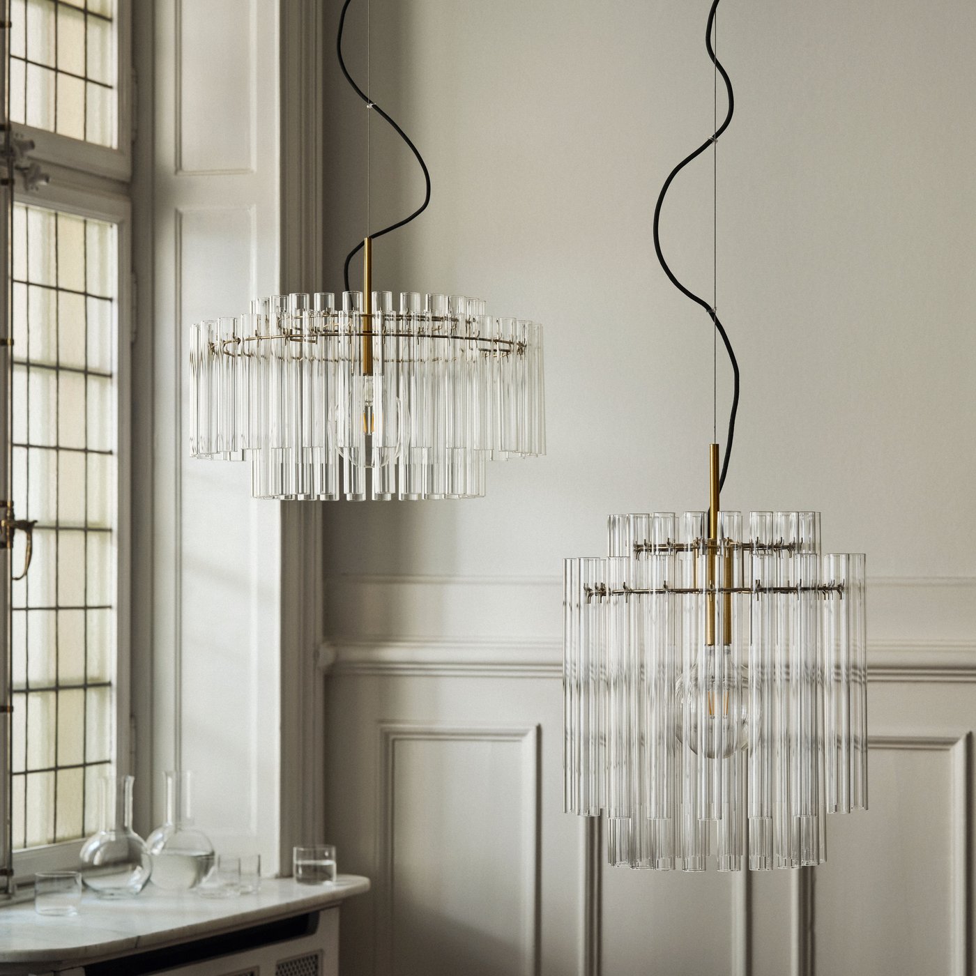 Två STOCKHOLM ljuskronor hänger från taket i ett rum med ljusa väggar.