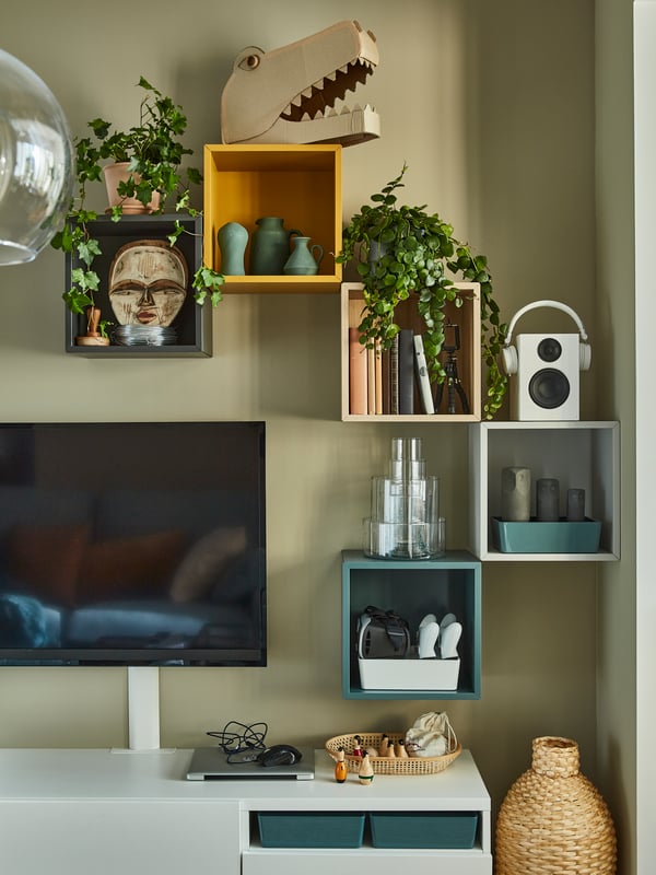 Five cube-like shelving units in black, yellow, beige, white and blue hang on the wall with decorative items in them.