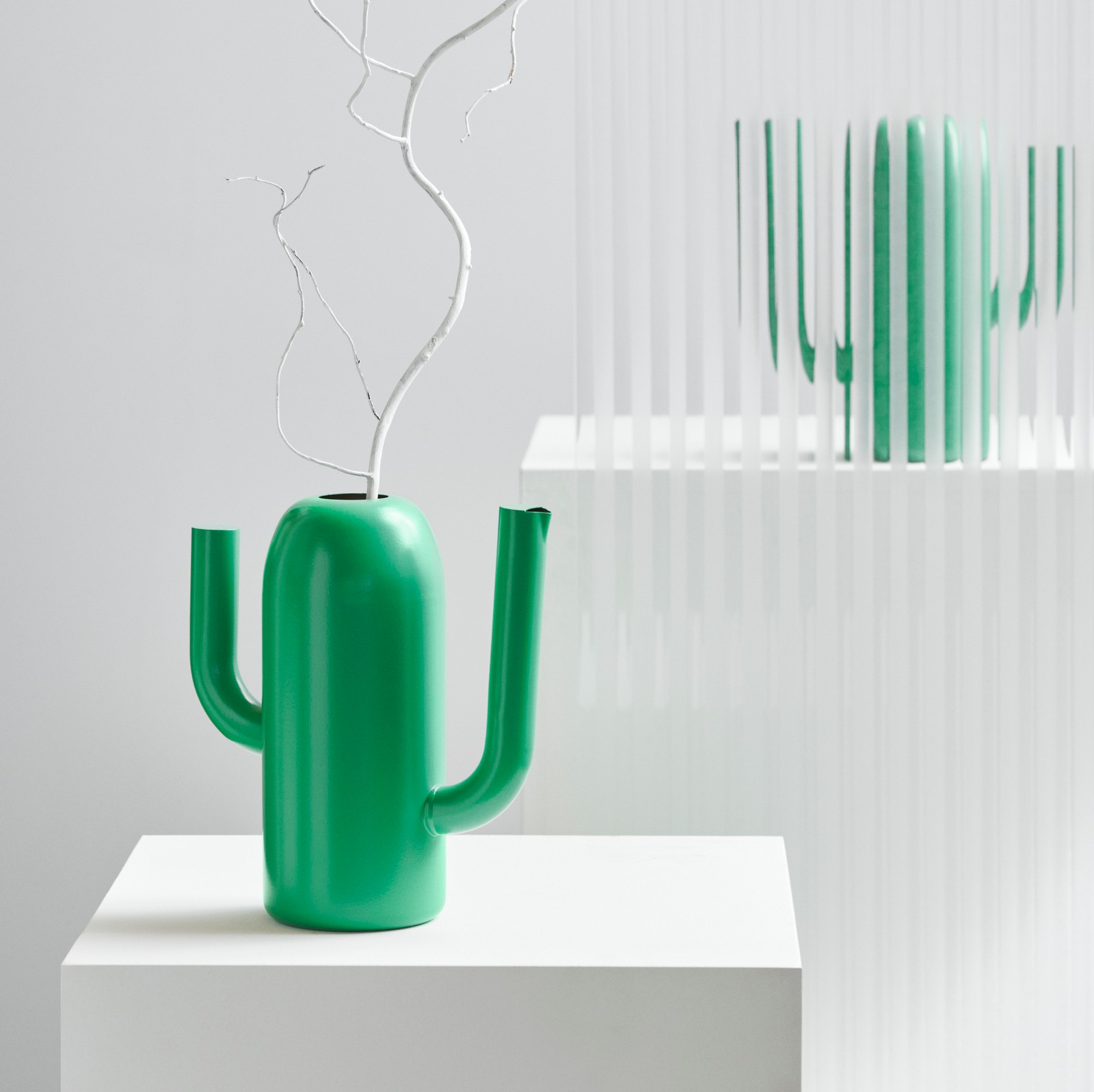 A bright green ÄRTBUSKE vase/watering can, shaped like a cactus, sits on a white box in a bright room.
