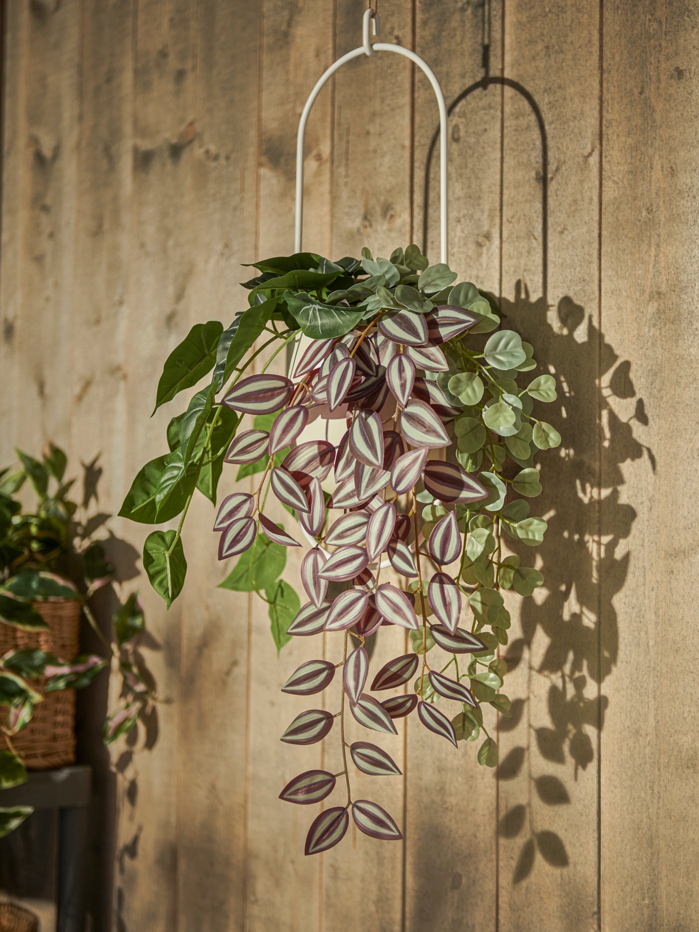 Umělá závěsná rostlina FEJKA v závěsném květináči CHILISTRÅN před dřevěnou stěnou v pozadí.