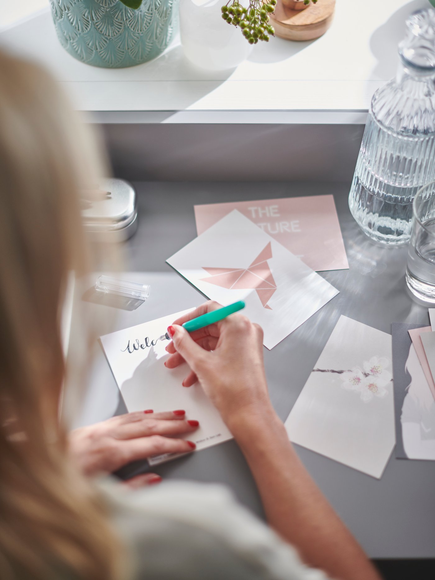 En person skriver på et lyserødt YLLEVAD kort, mens hun sidder på sit hjemmekontor.