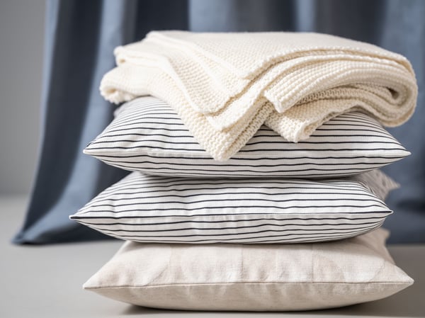 Image of three stacked cushions with a cream throw on top