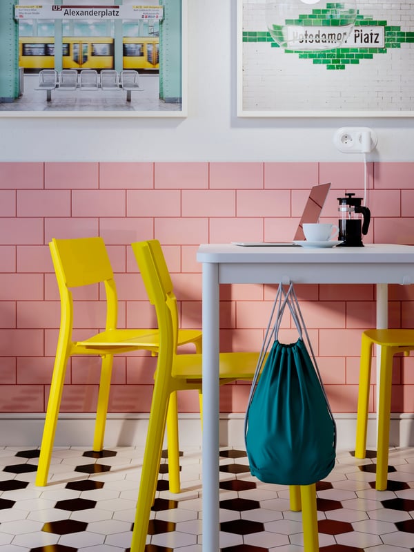 Part of a restaurant with tiled floor and pink-tiled walls with yellow JANINGE chairs at a white TOMMARYD table.