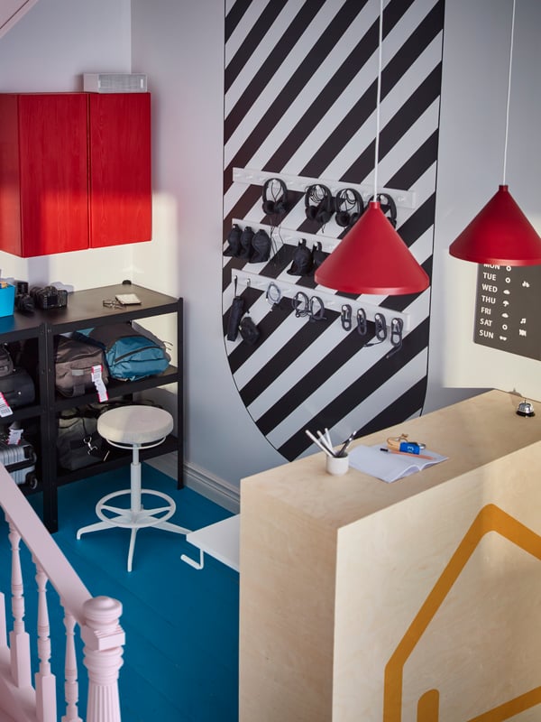 An entrance area with a reception desk in light wood, two red lamps hanging above it and plenty of smart storage.