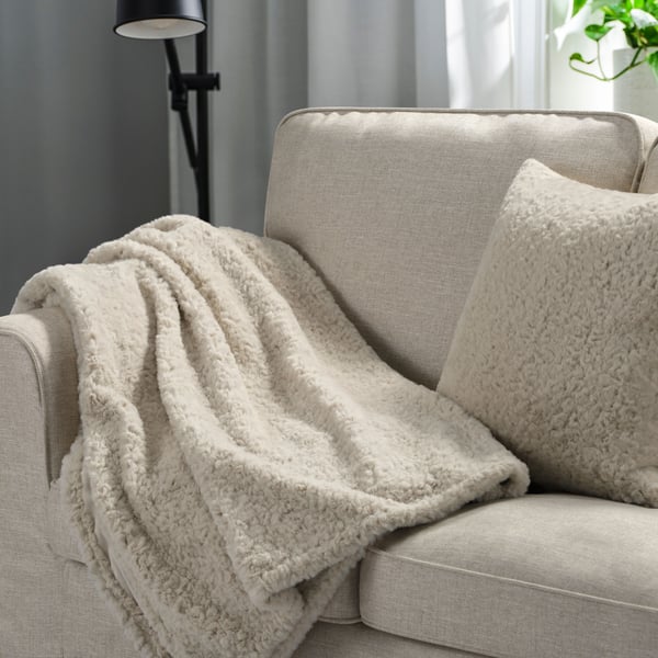 Fluffig vit kudde och pläd i beige soffa.