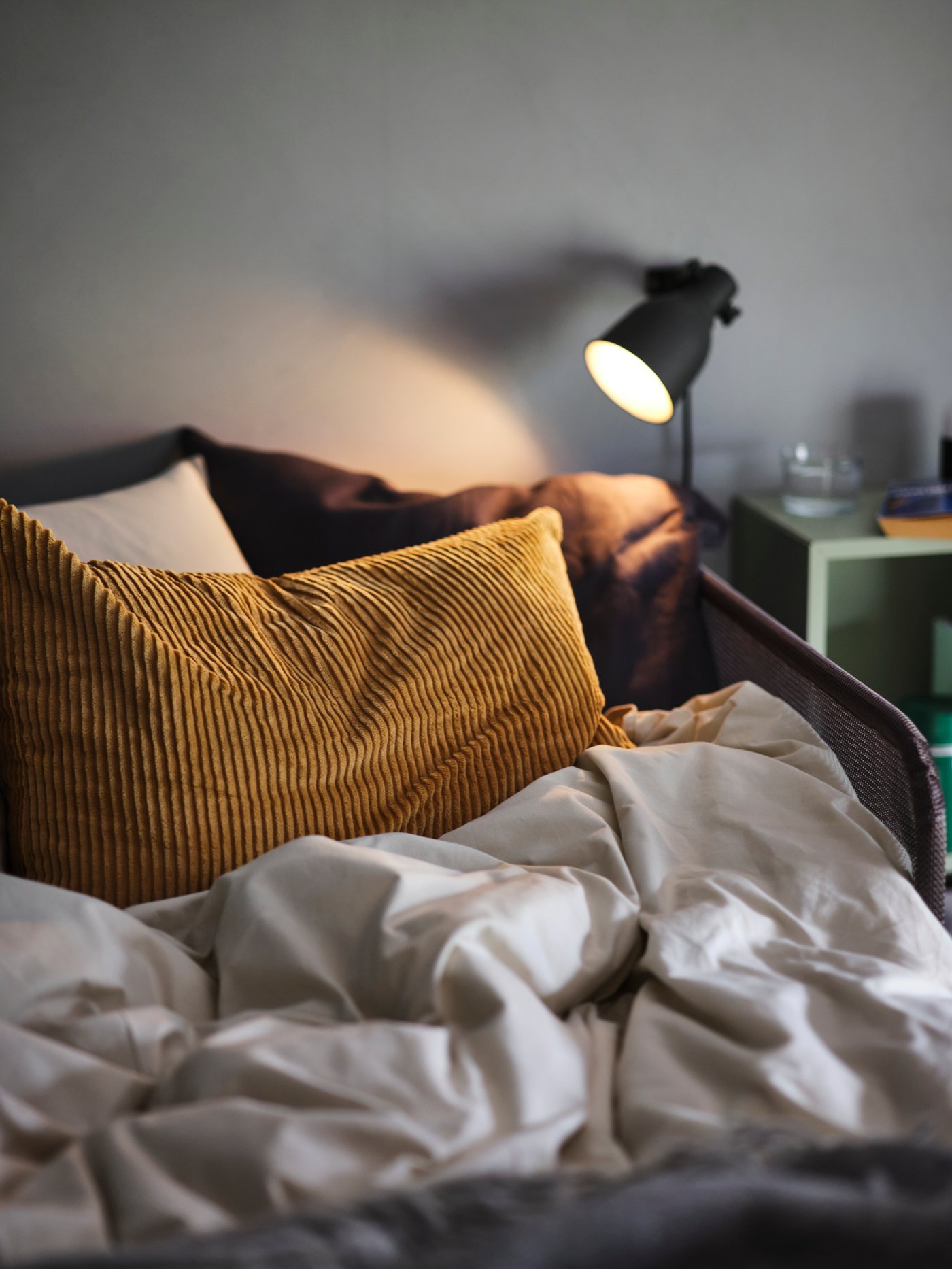 Lámpara de dormitorio sobre cama con cojín color dorado ÅSVEIG.