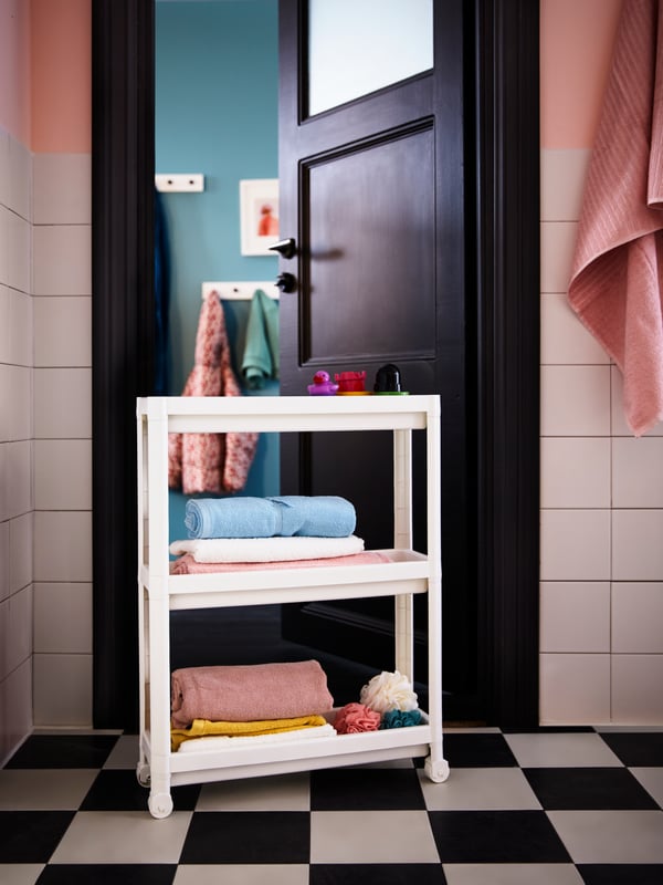 White VESKEN trolley holding several bath towels and accessories and light pink VIKFJÄRD bath towel at entrance of bathroom.