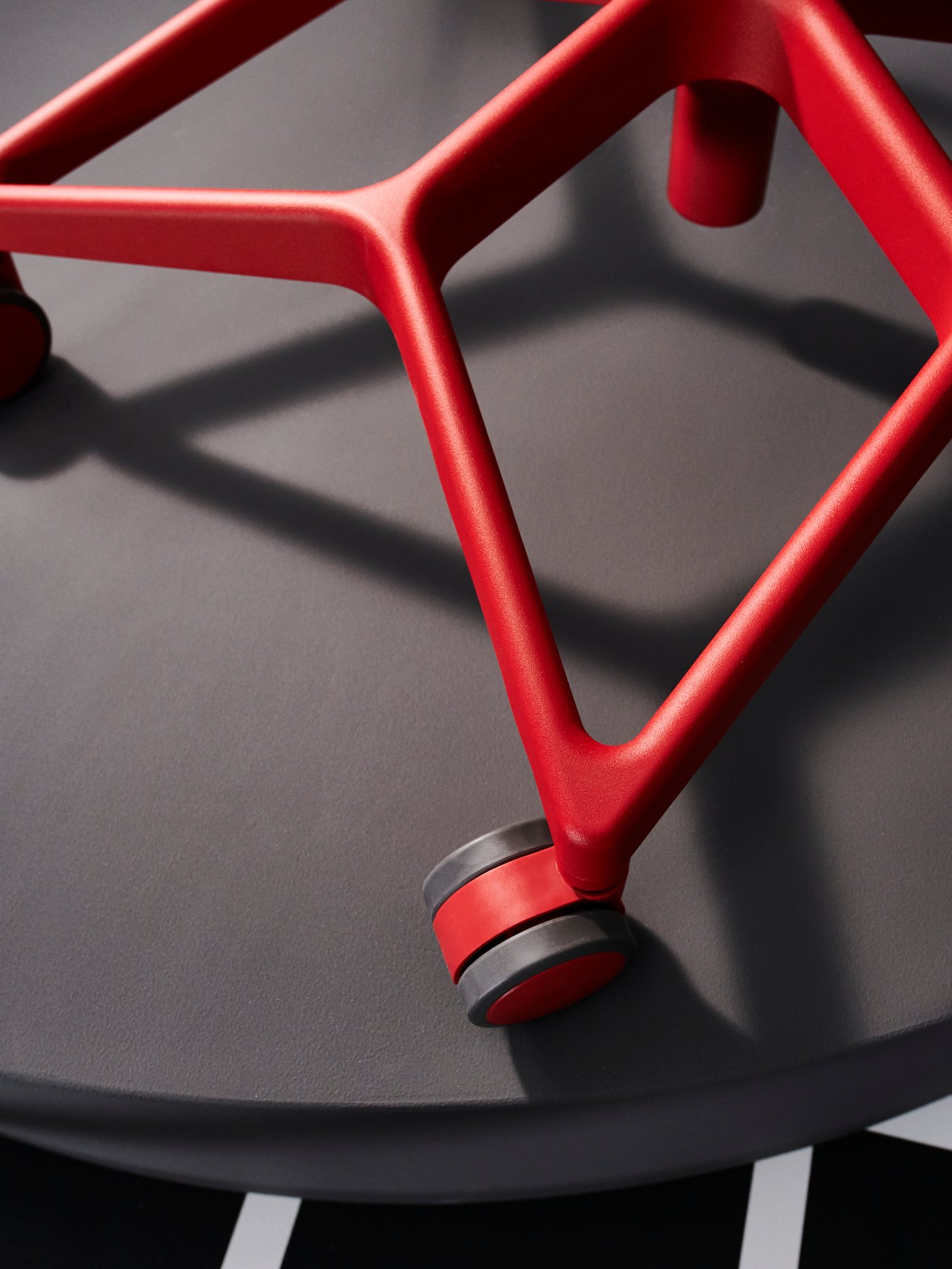 Un espacio de trabajo moderno que incluye una silla de juego gris con ruedas rojas, unidas por barras de acero a juego.