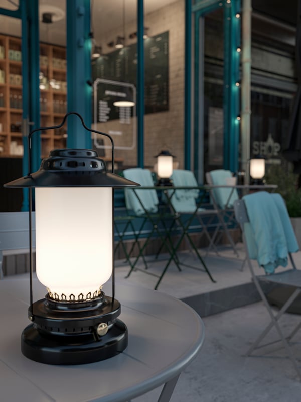 STORHAGA LED lamps on top of grey SUNDSÖ tables outside a café with light blue THORGUN throws on the back of the chairs.