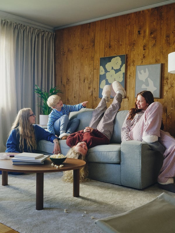 Three children lounge on a KIVIK two-seat Tibbleby beige/grey sofa. One child is upside down, reaching toward a low table.
