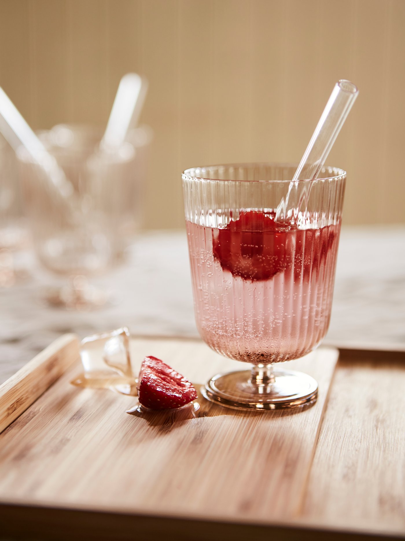 An ANLEDNING goblet glass with a ridged pattern, holding a pink drink, strawberries and a glass straw.