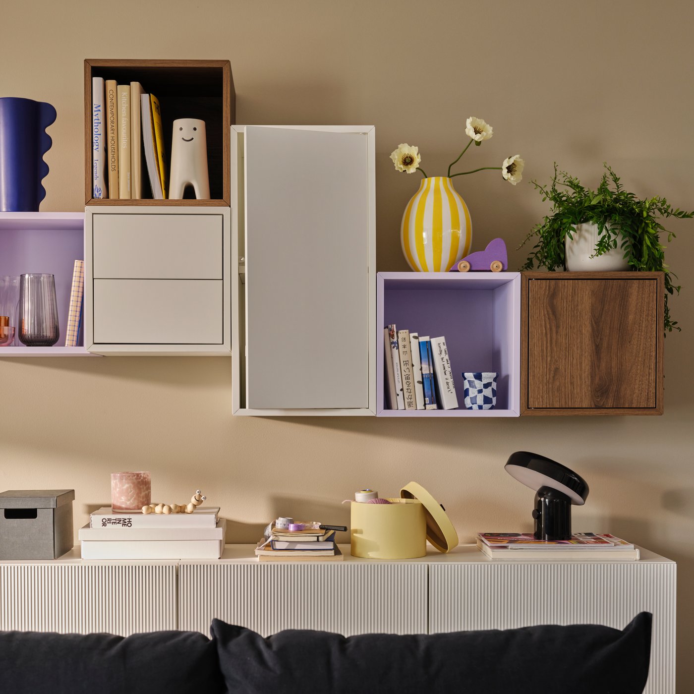 A light living room with an asymmetric arrangement of EKET and BESTÅ wall cabinets, holding books and decoration. 