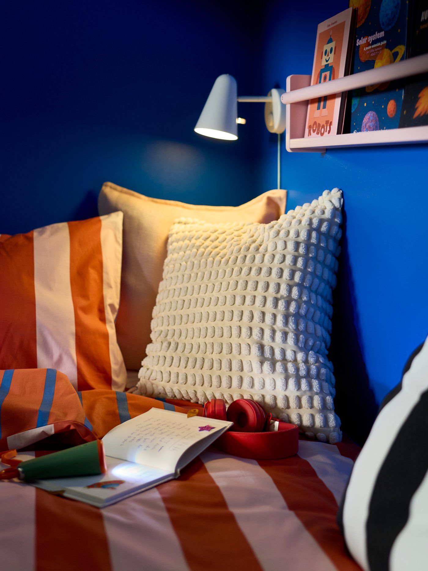 Juego de funda de duvet y funda de almohada BARNDRÖM sobre una cama infantil, junto a una pared azul con lámpara de lectura y una repisa pequeña.