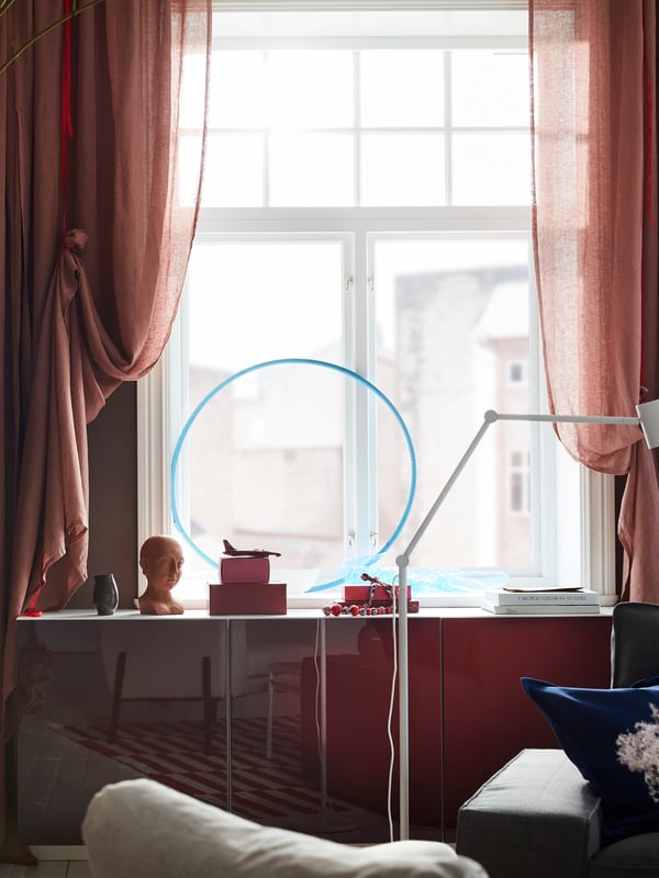 Light brown-pink LEJONGAP curtains are draped with red ribbons and hang by a window where the light shines in beautifully.