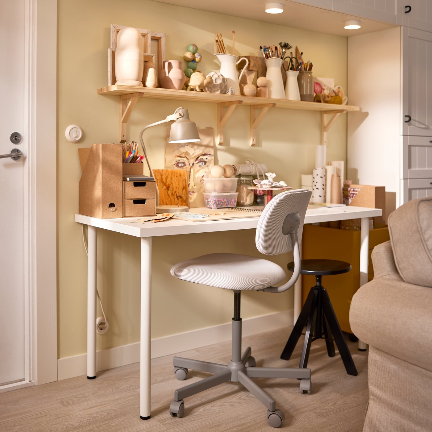 A BLECKBERGET swivel chair and a RUDSTORP stool stand at a LAGKAPTEN/ADILS desk underneath two wall shelves.