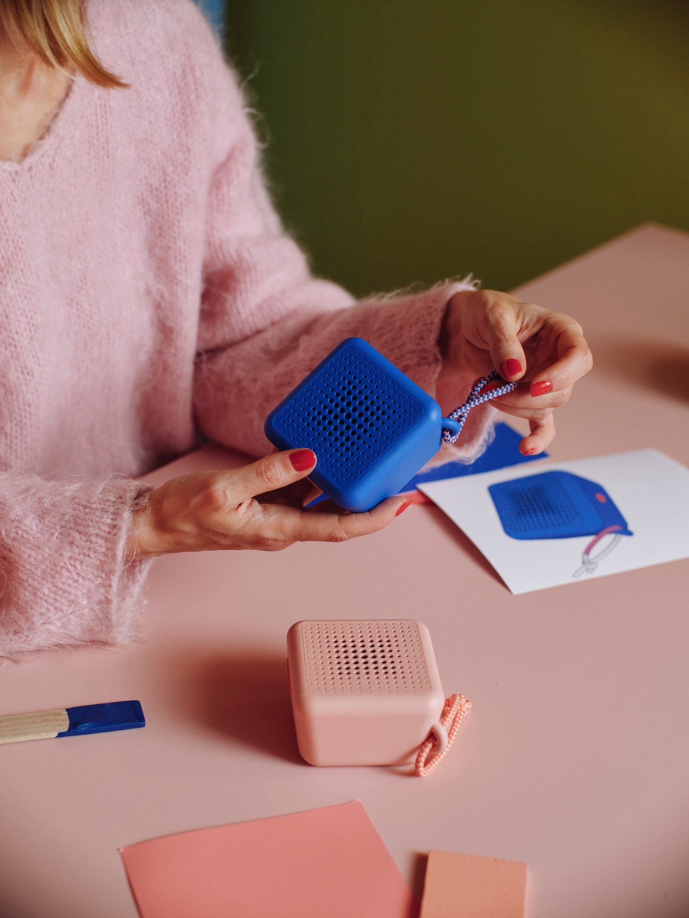 Green KULGLASS Bluetooth speaker lamp glowing with soft light on a side table, with a hand using the BILRESA remote to control it.