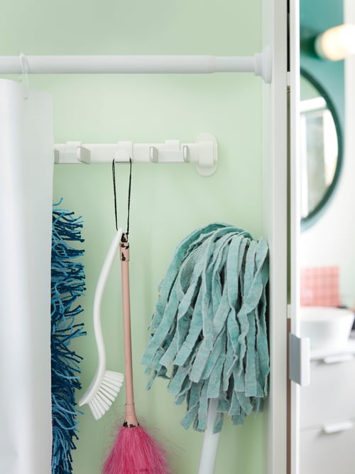 Detail shot of a modern bathroom with green tiles, a white shower curtain rod and a rack with seven hooks.