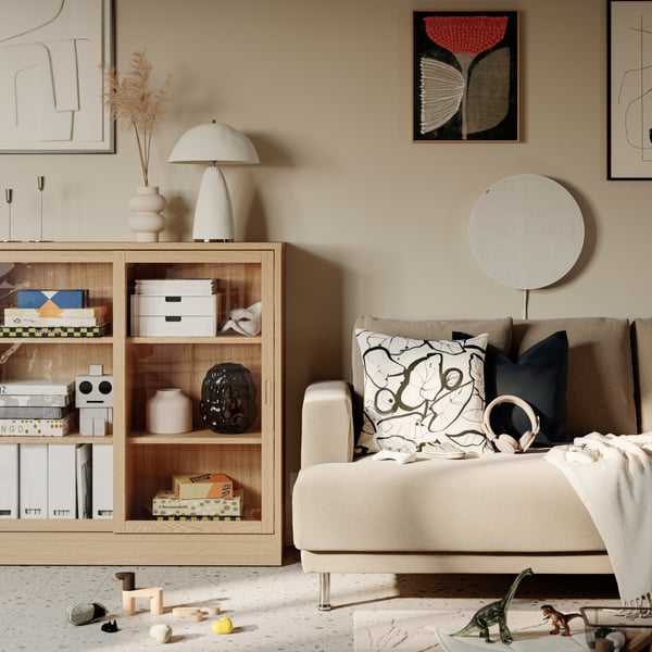 A TONSTAD cabinet with sliding glass doors beside an UPPÅKRA 3-seat modular sofa. A Bluetooth speaker is mounted on the wall.