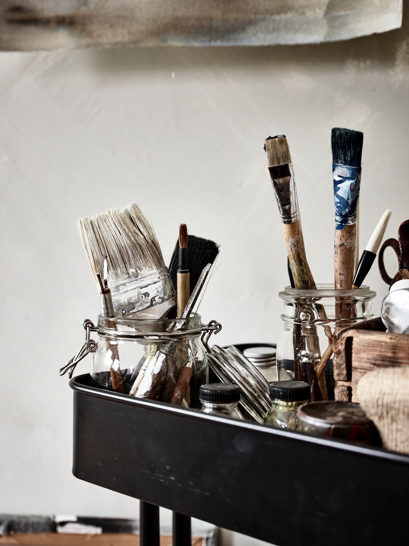 Une desserte noire sur laquelle y sont rangés des bocaux avec couvercle KORKEN contenant des pinceaux utilisés.