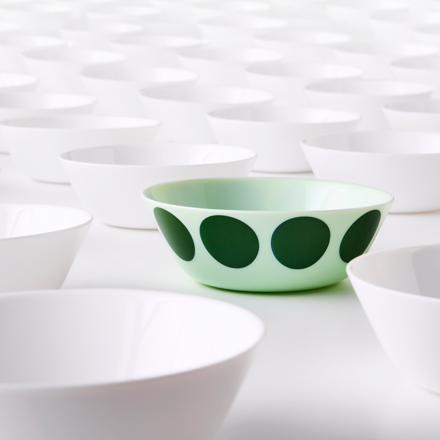 Light green OFTAST bowl with large green dots among a collection of white bowls.
