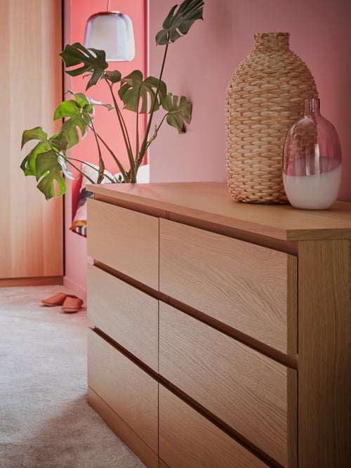 A pink room that has a MALM chest of drawers in white stained oak veneer with six drawers and two vases on top.