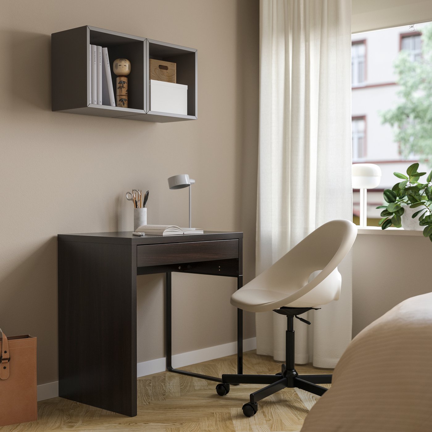 Un escritorio MICKE negro con una lámpara de escritorio. Delante del escritorio una silla con ruedas.