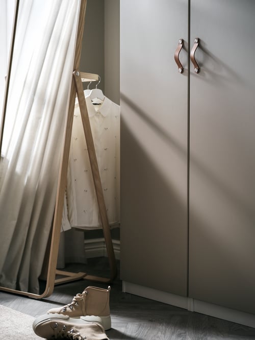 Bedroom dresser with two beige doors made out of particleboard with two beige leather handles, next to a rectangular mirror.