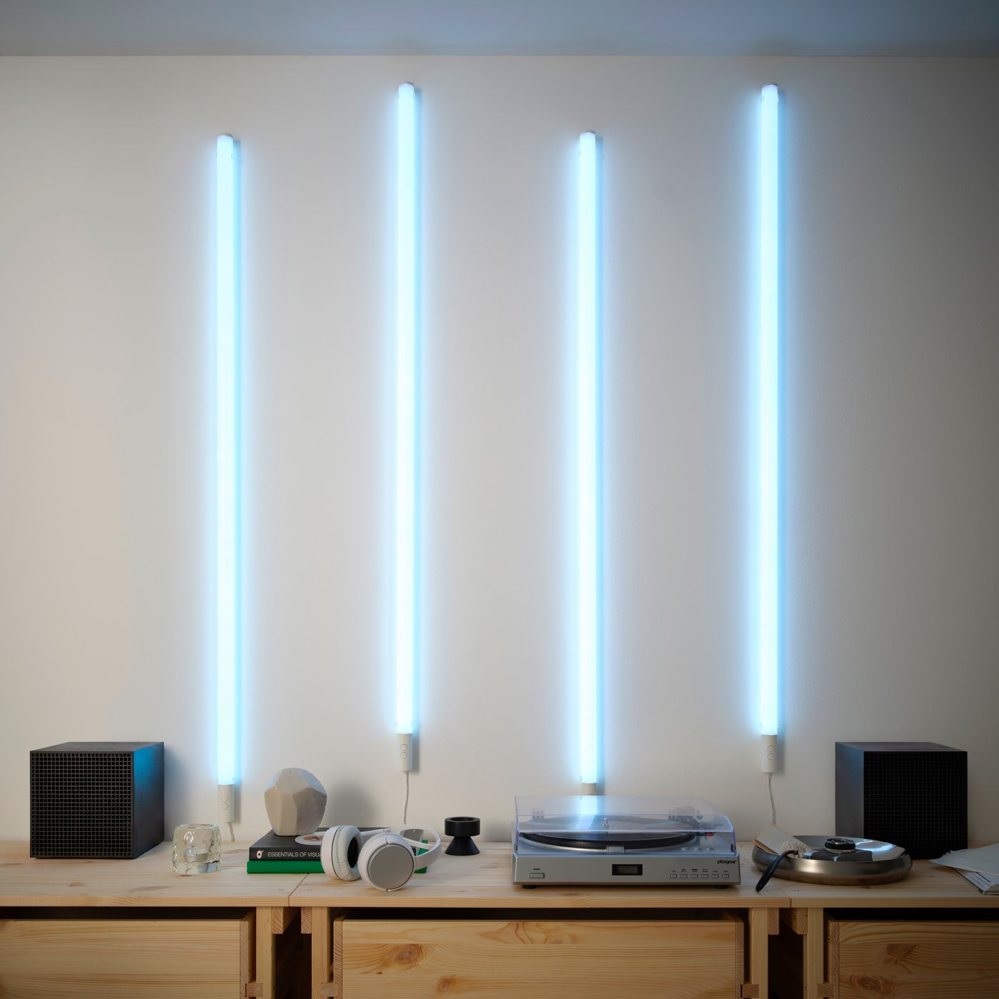 Four FÖRLIG LED floor/wall lamps with a light blue glow, mounted vertically on a wall over a wooden sideboard.