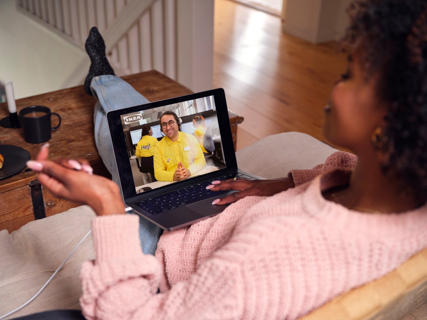 Someone wearing a pink sweater is talking via a tablet with an IKEA co‑worker about designing their own BESTÅ storage unit.