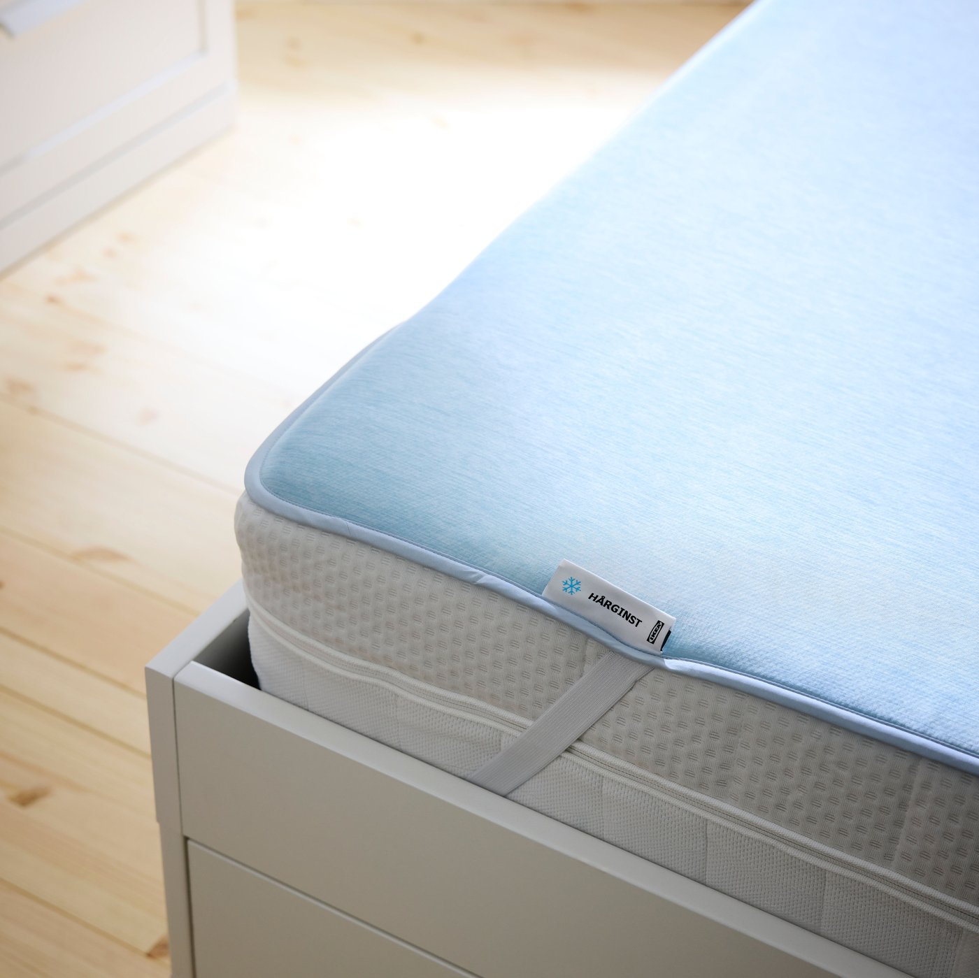Detailný záber na chladiaci chránič matraca HÅRGINST na vrchu matraca v drevenom ráme postele.