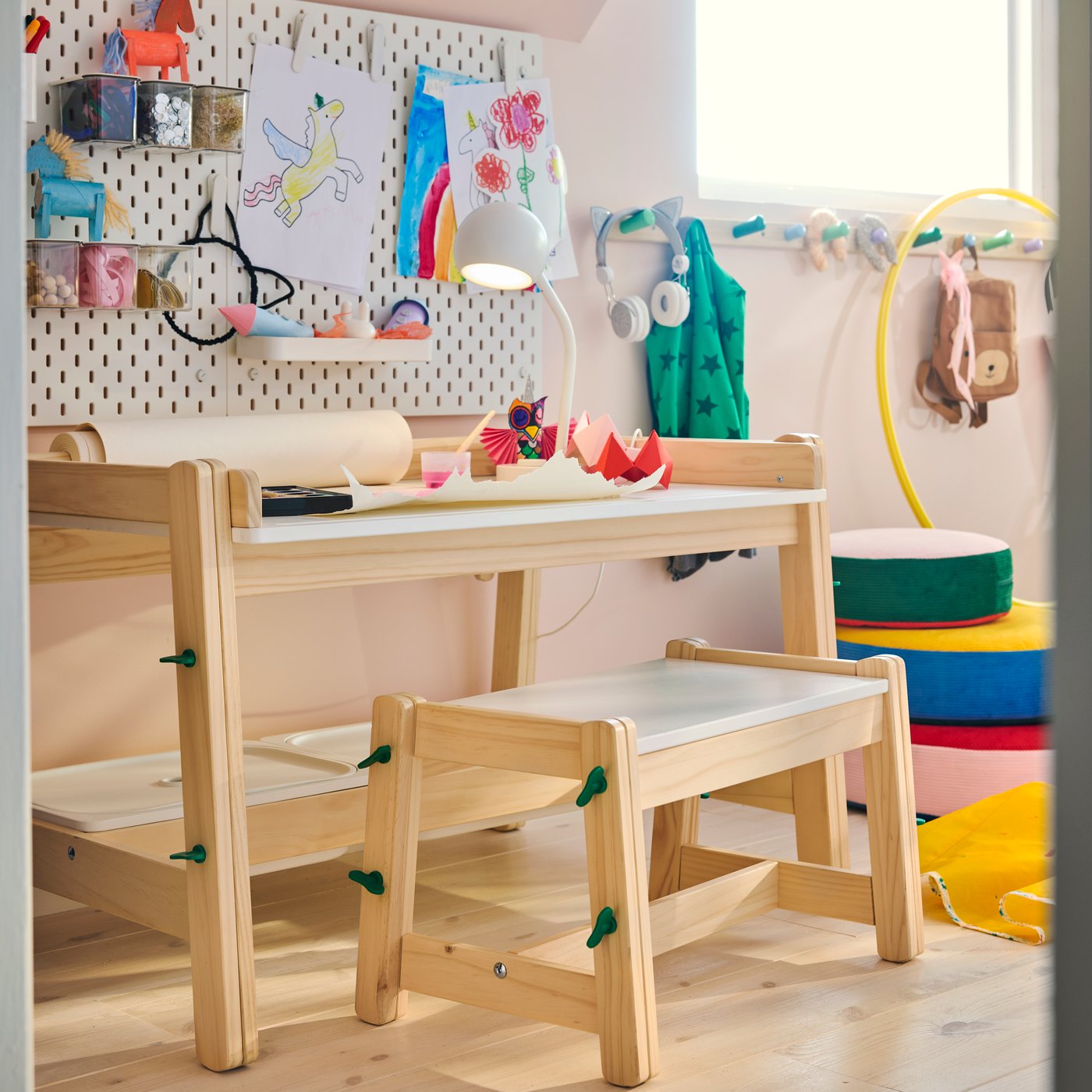 Un escriptori FLISAT amb caixes de pi amb un banc a joc, en una habitació infantil al costat d'una paret de tauler amb obres d'art.