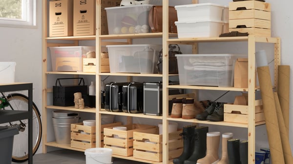 Een houten IVAR stellingkast in de garage of berging met houten KNAGGLIG opbergboxen en kunststof SAMLA dozen met sportspullen of andere spullen erin.