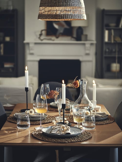 Dining area with a candlestick set with candles, a goblet, glasses, white wine glasses and place mats all set on a table.