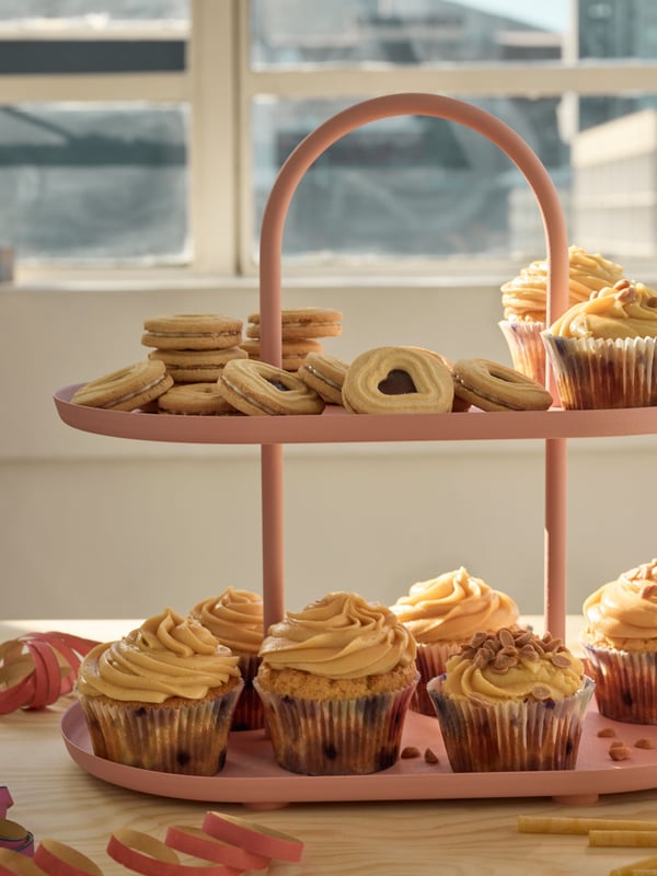 Eine rosa Etagere mit Keksen und Cupcakes.