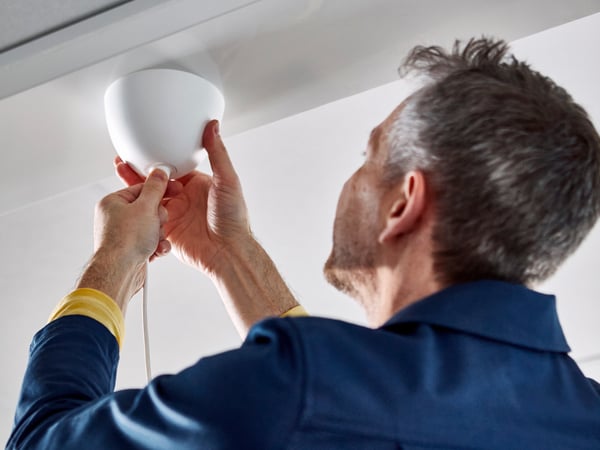 Een IKEA medewerker staat met zijn rug naar de camera en verstelt een lampenkap aan het plafond.