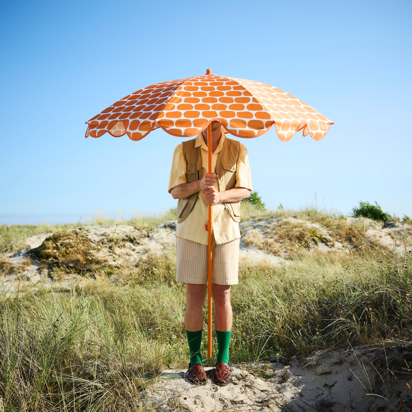 A beach scene with a person holding a bright orange STRANDÖN parasol clearly displaying its dotted pattern.