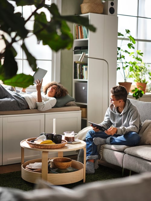 Two teens relaxing in a living area, with one sitting behind a birch veneer BORGEBY coffee table on a SÖDERHAMN 3-seat sofa.