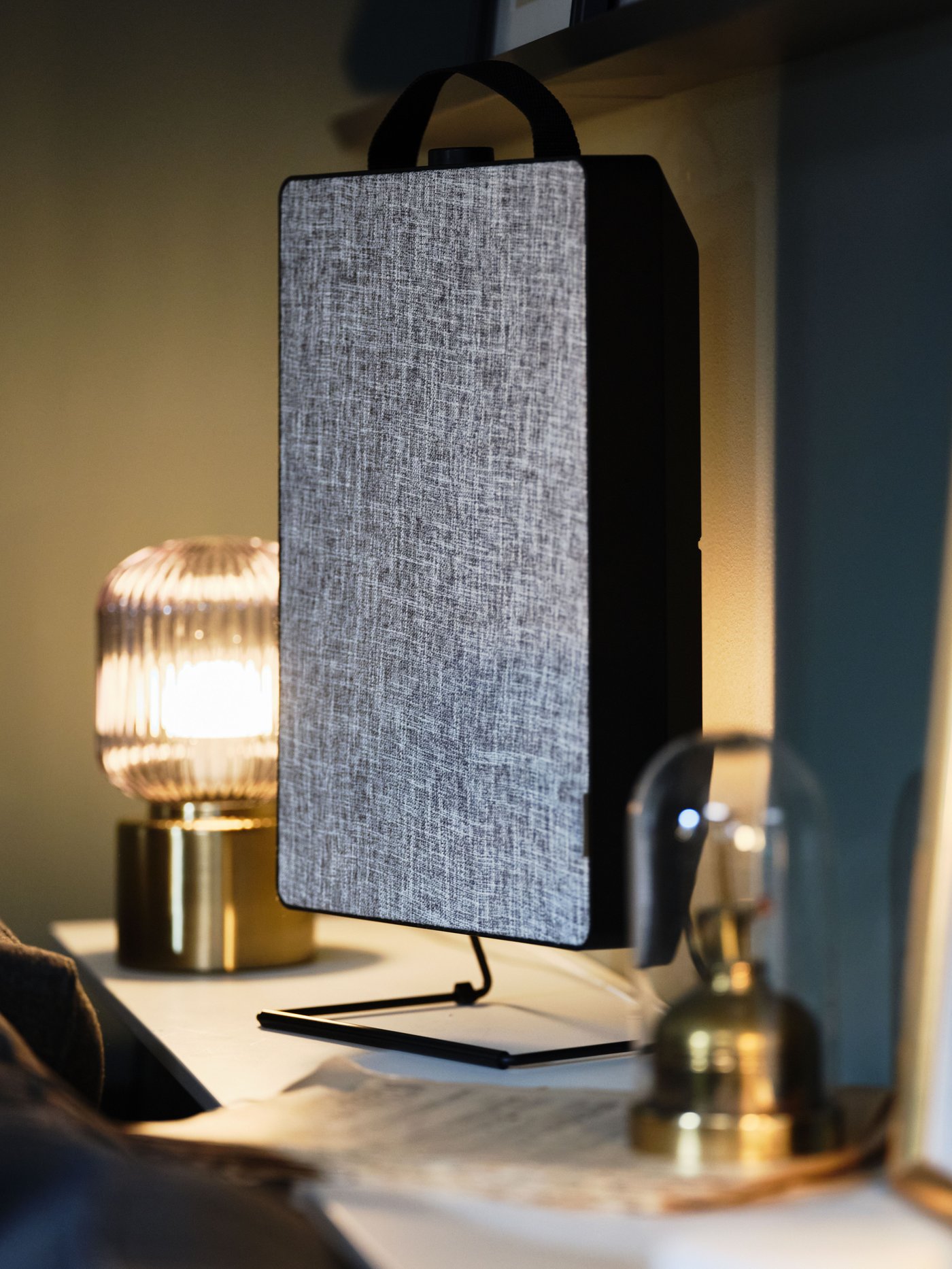 A black FÖRNUFTIG air purifier stands in-between two brass/grey clear glass SOLKLINT table lamps on a white wall shelf.