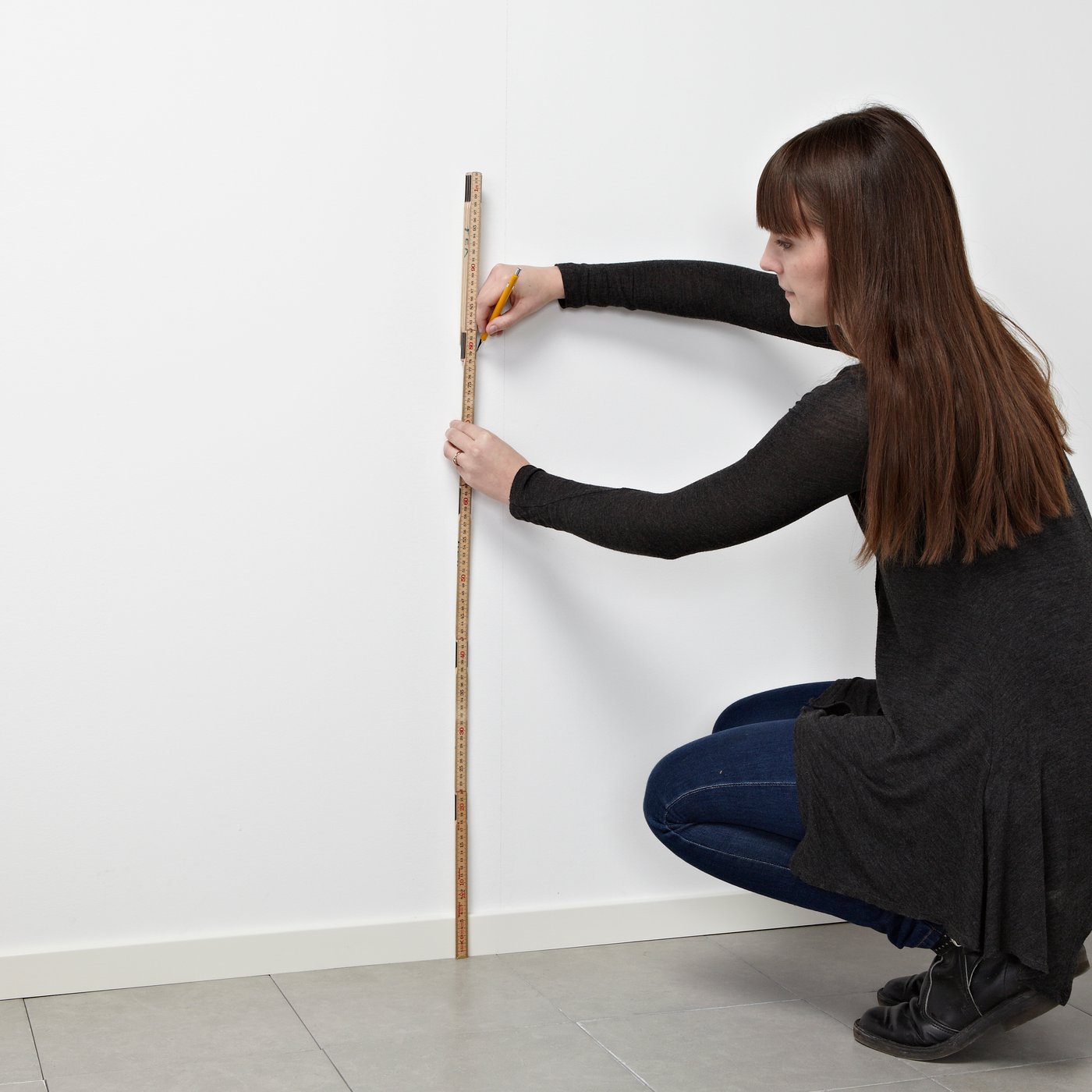 Una mujer tomando medidas con un metro en la pared.