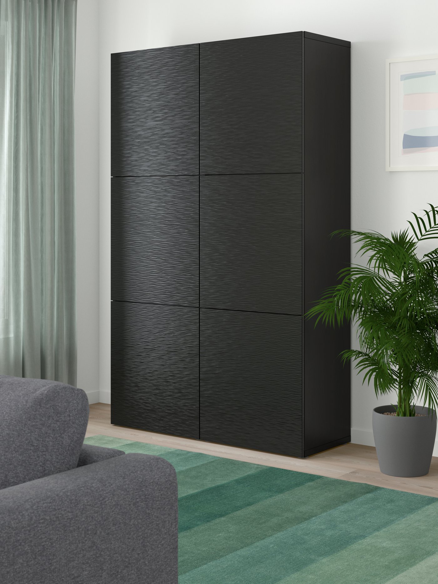 Dans un salon, une combinaison de rangement BESTÅ noir-brun/Laxviken noir avec portes. Un tapis vert et un canapé gris.