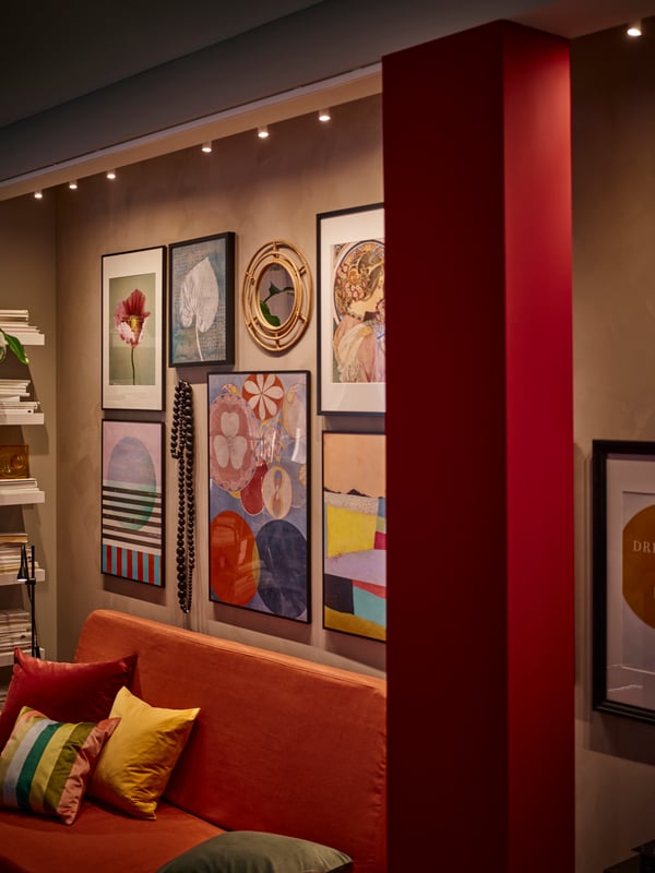 A wall with different sizes of black LOMVIKEN frames with BILD posters in it above an orange NYHAMN sofa bed.