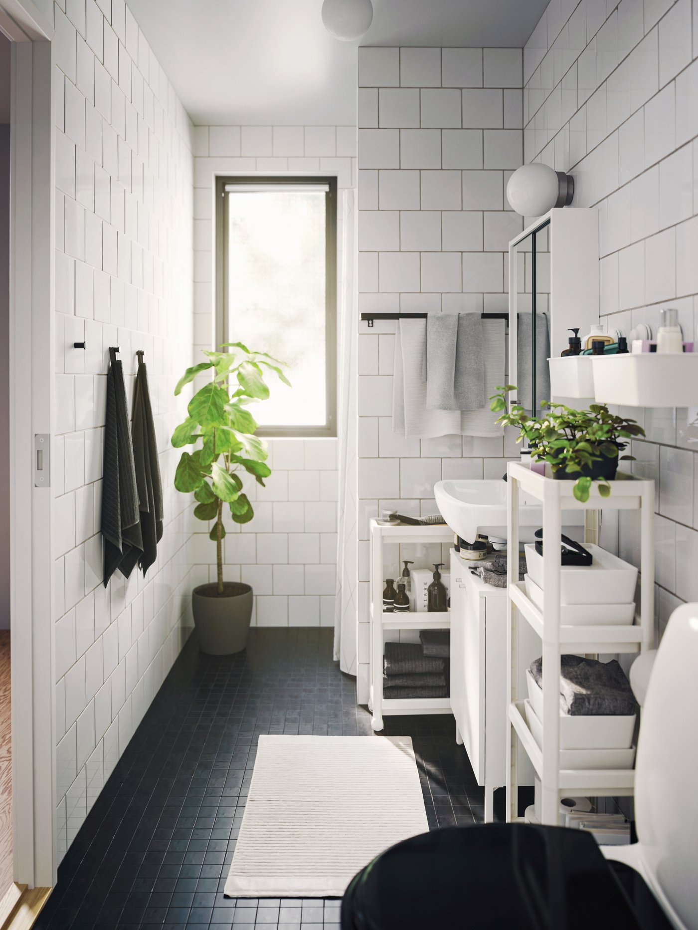 Baño con una estantería blanca de polipropileno junto a una alfombra rectangular y un carrito blanco.