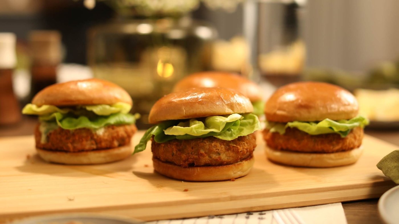 Four crispy shrimp sandwiches with lettuce on buns arranged on a wooden board.