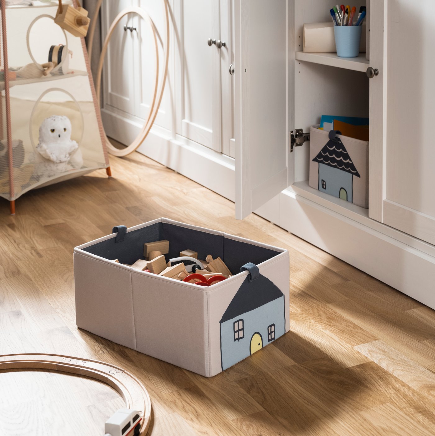 A BARNDRÖM box with toys in it and a toy railway on the floor in front of a HAVSTA storage combination with one door open.