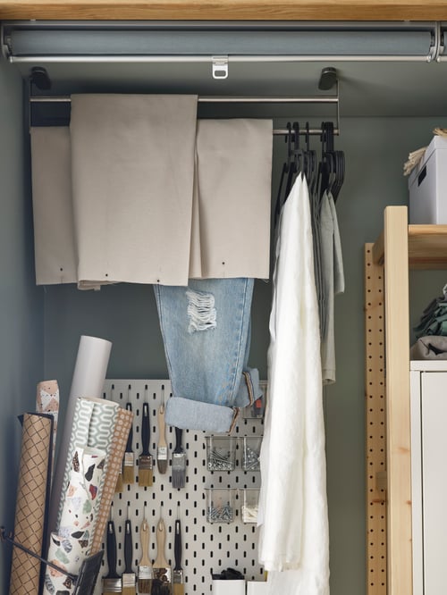 Spațiu de lucru modern focalizat pe o balustradă gri pentru prosoape realizată din oțel inoxidabil care susține mai multe umerașe în fața unui pegboard alb.