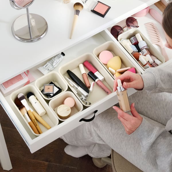 A bedroom with a white BRYTNING desk made from white material. It holds cosmetics and a mirror on top.