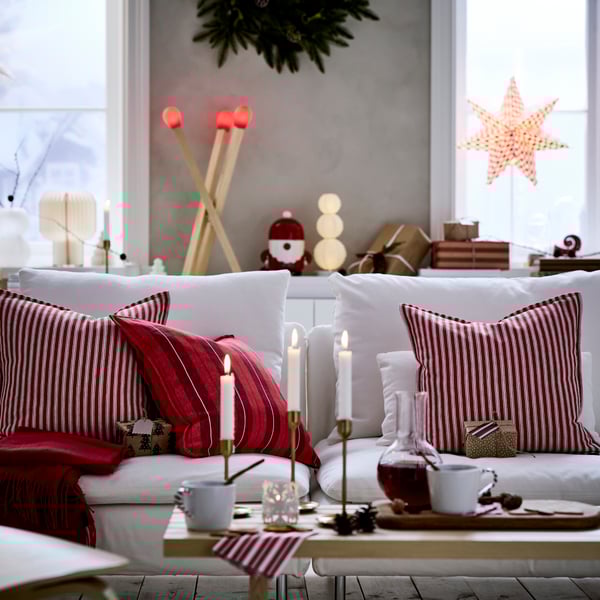 Three red-striped VINTERFINT cushion covers are on a sofa, in a living room that is decorated for Christmas.