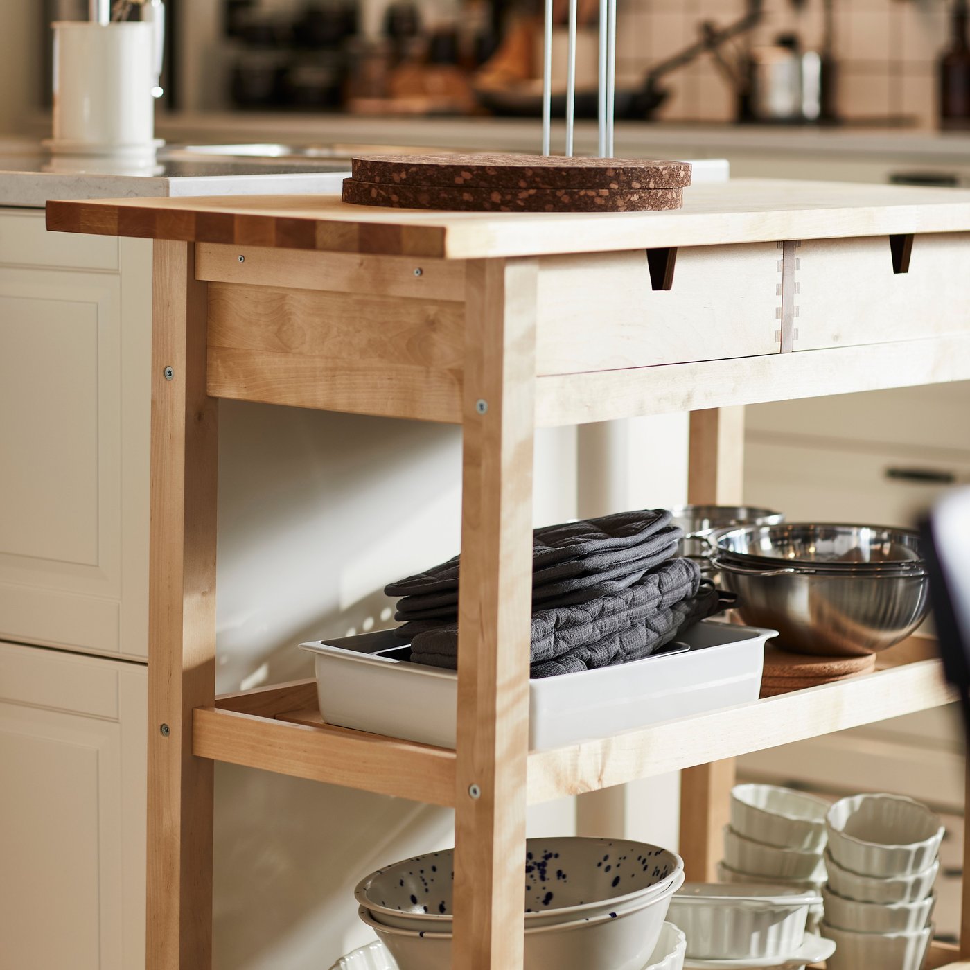 A bright kitchen has a FÖRHÖJA kitchen trolley with various kitchen items stored on the shelves and on the worktop.